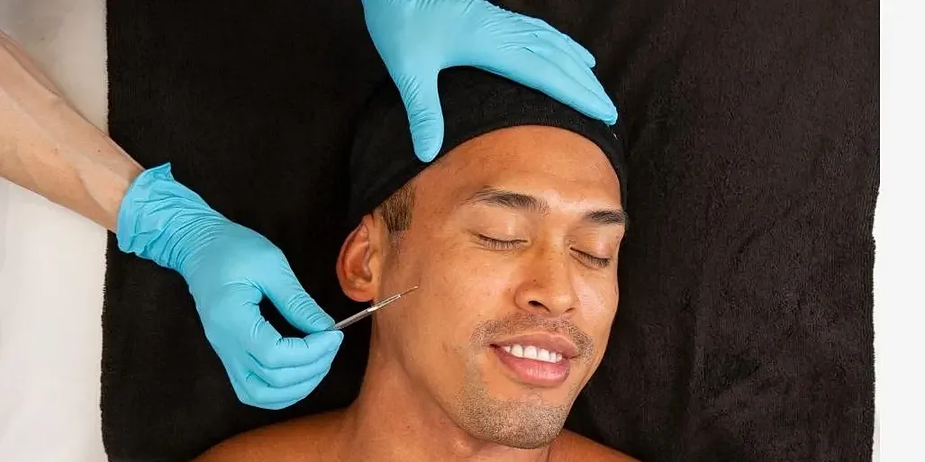 Man receiving skincare treatment with gloved hands.
