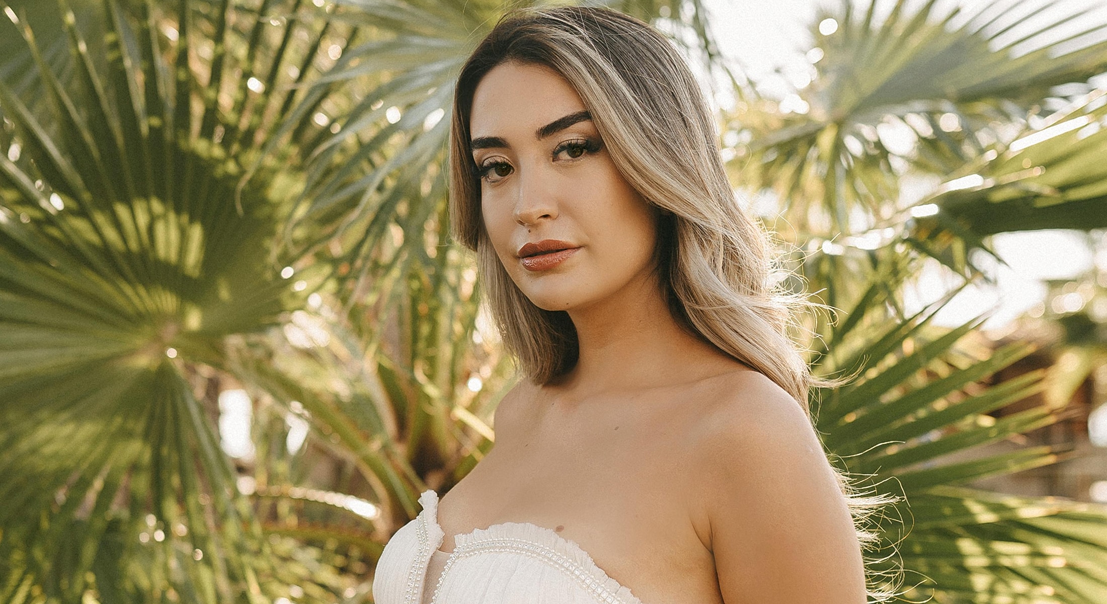 Woman in white dress amidst lush greenery.