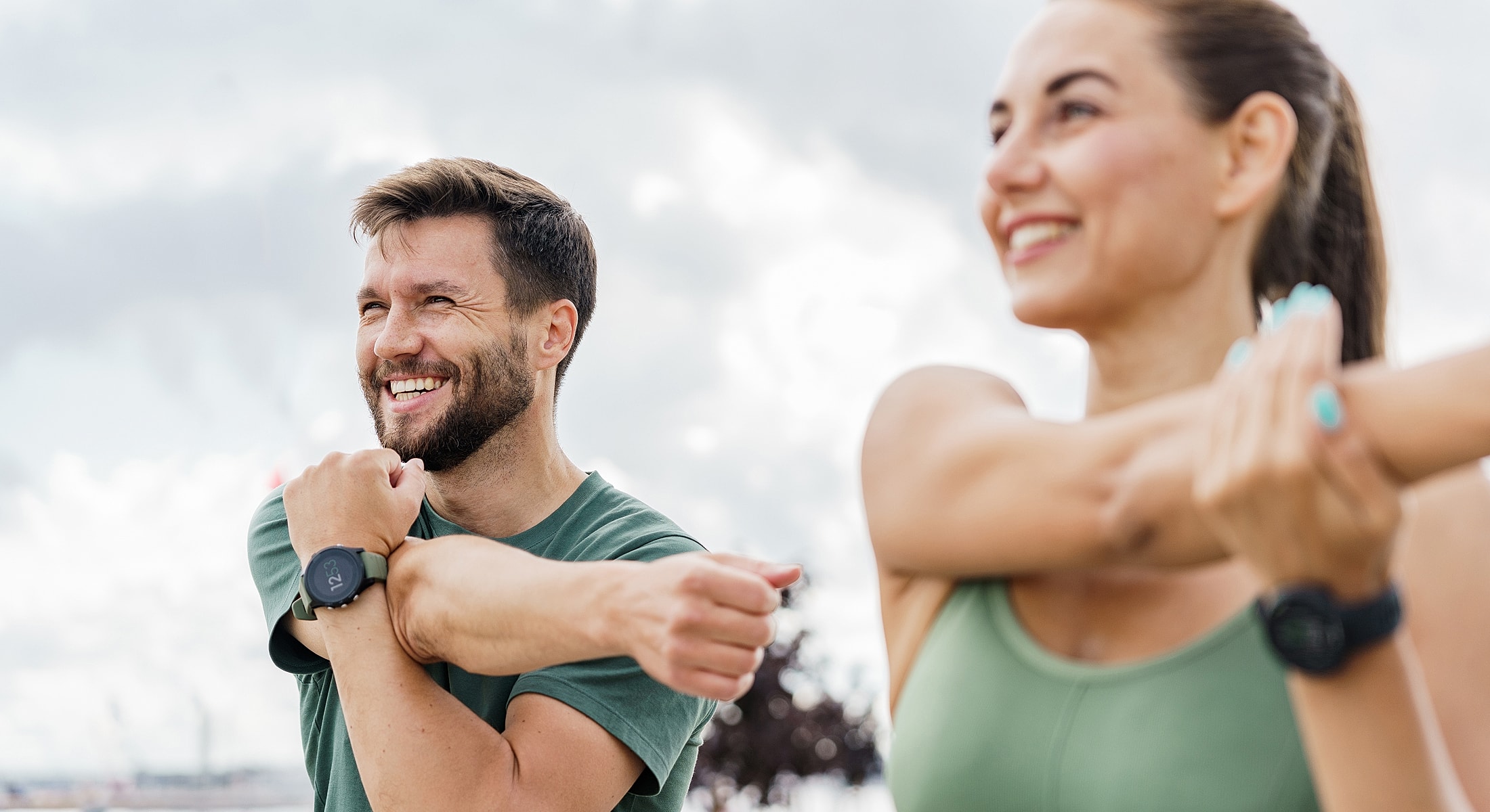 Smiling individuals stretching outdoors during workout.